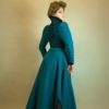 woamn wearing a teal blue late victorian dress with high standing collar and black velvet accents